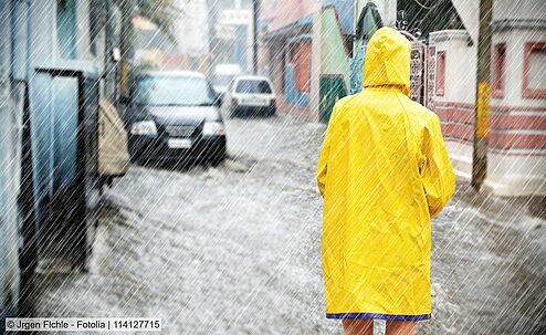 Person im Regenmantel vor Straße mit Hochwasser